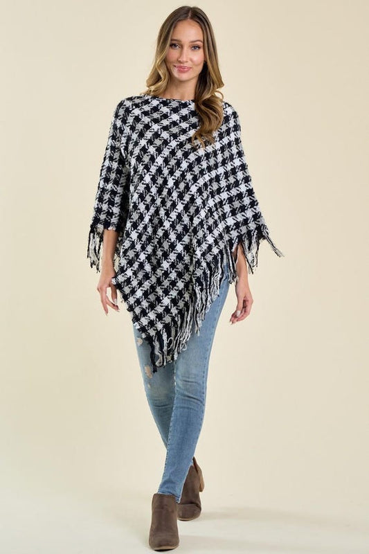 Women's black and white houndstooth print knit poncho with an asymmetric drape and fringe trim.