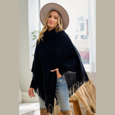 Front view of a black cowl neck poncho with an asymmetrical fringe trim and soft acrylic knit texture