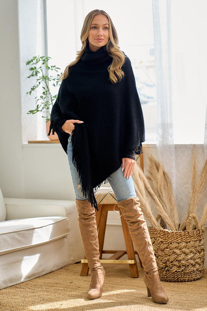 Rear view of this black knit poncho showing the flowing drape and long bohemian fringe hemline