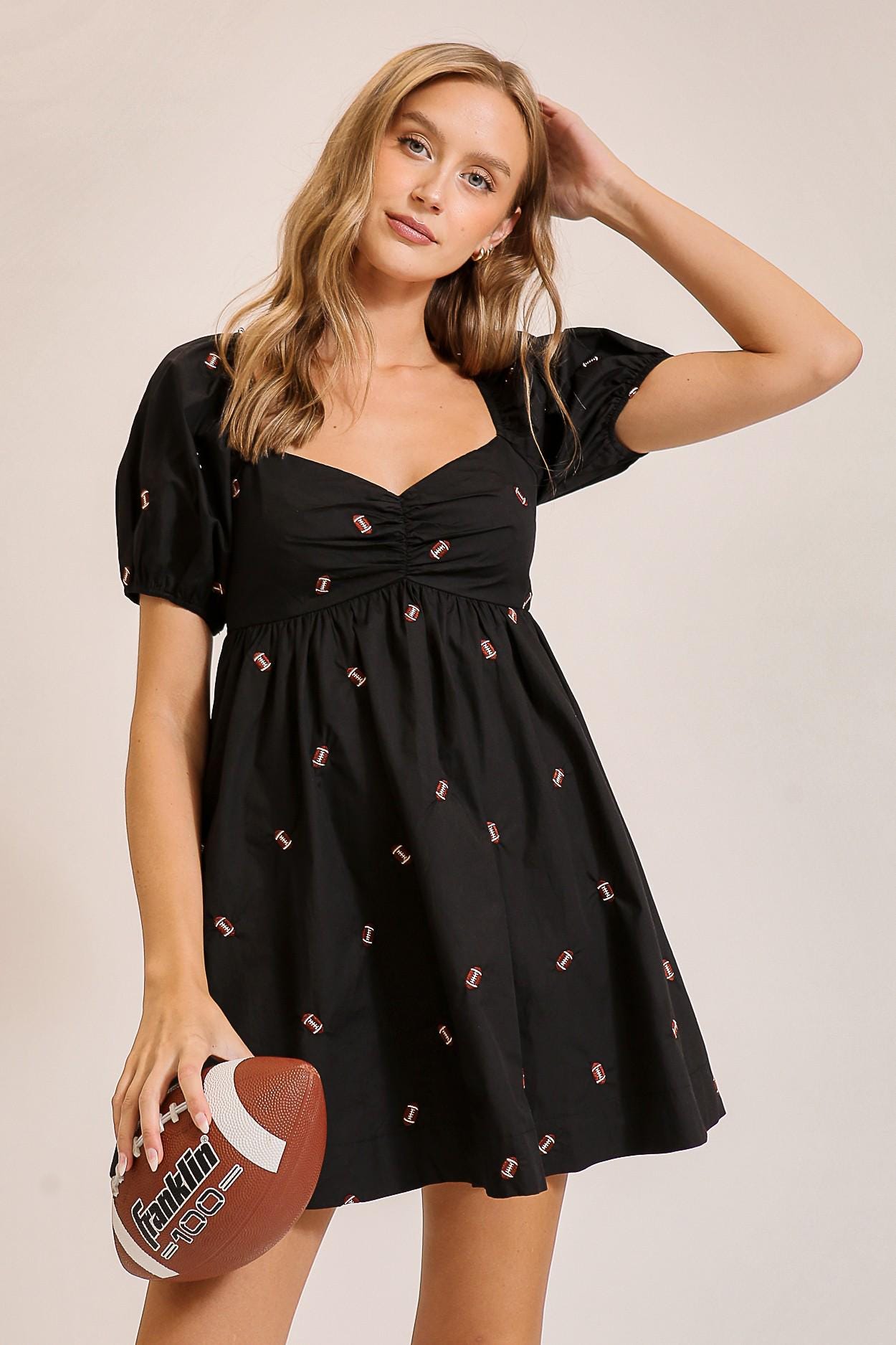 Front view of a black football print babydoll mini dress with ruched sweetheart neckline and puff sleeves