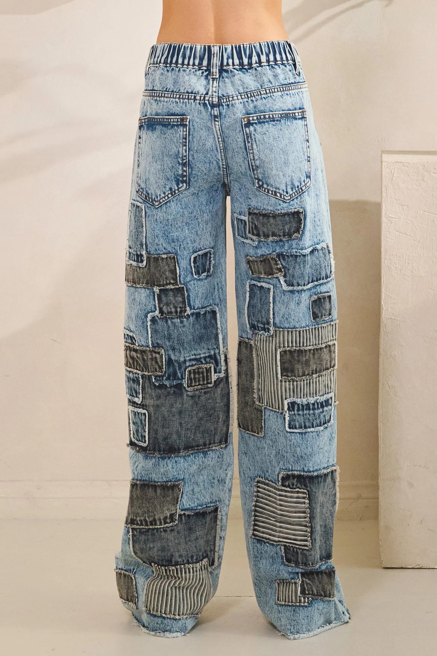 Wide leg opening of blue acid wash jeans with eclectic upcycled-style fabric patches