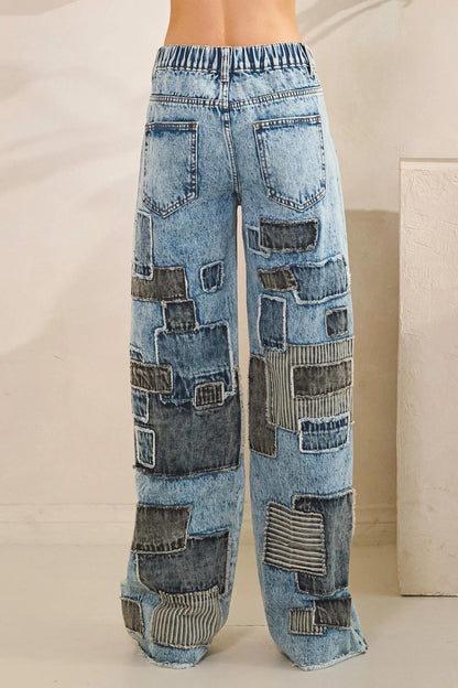 Wide leg opening of blue acid wash jeans with eclectic upcycled-style fabric patches
