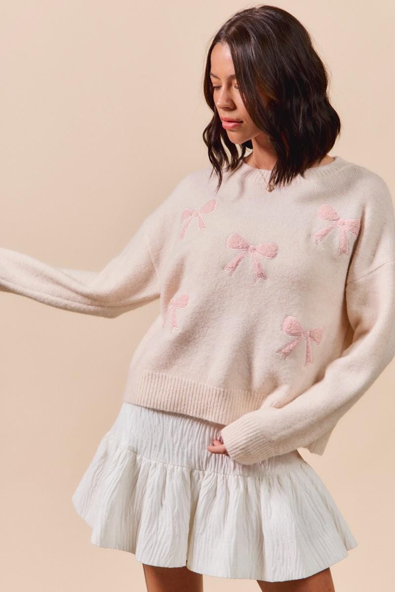 Back of the cream coquette sweater showing pink ribbon embroidery on a textured knit base
