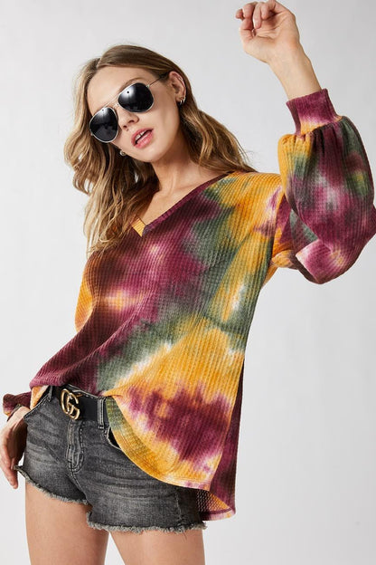Lifestyle shot of a model wearing the mustard tie dye v-neck top styled off-the-shoulder for streetwear.