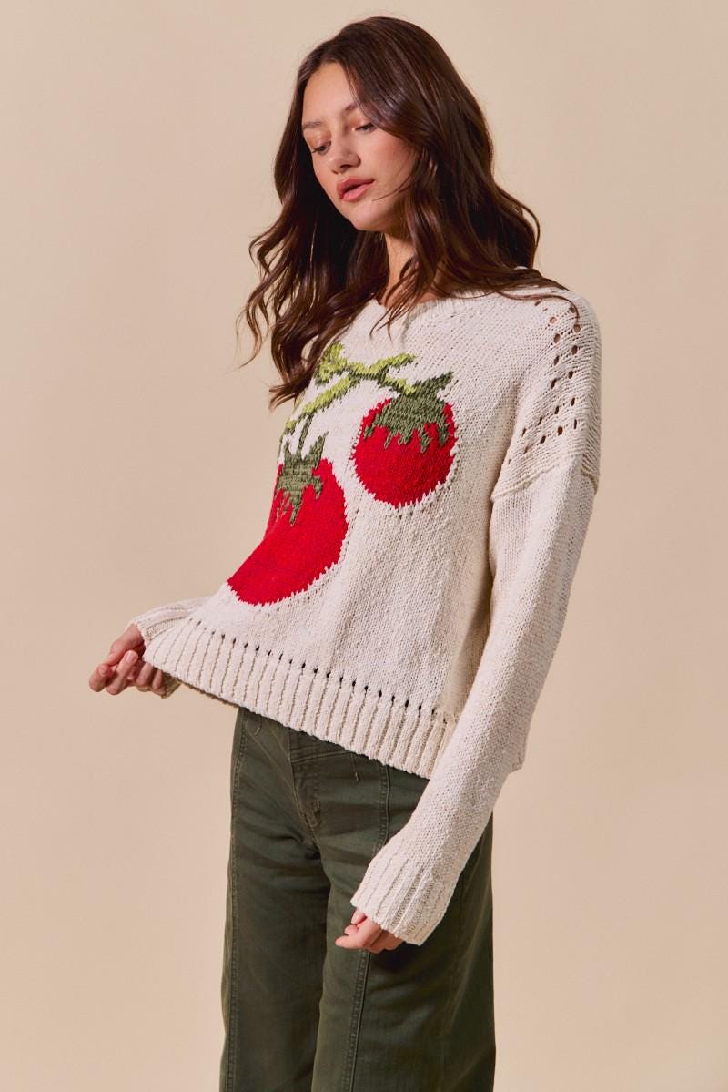 Lifestyle shot of a model wearing the gardencore tomato sweater in a lush outdoor setting