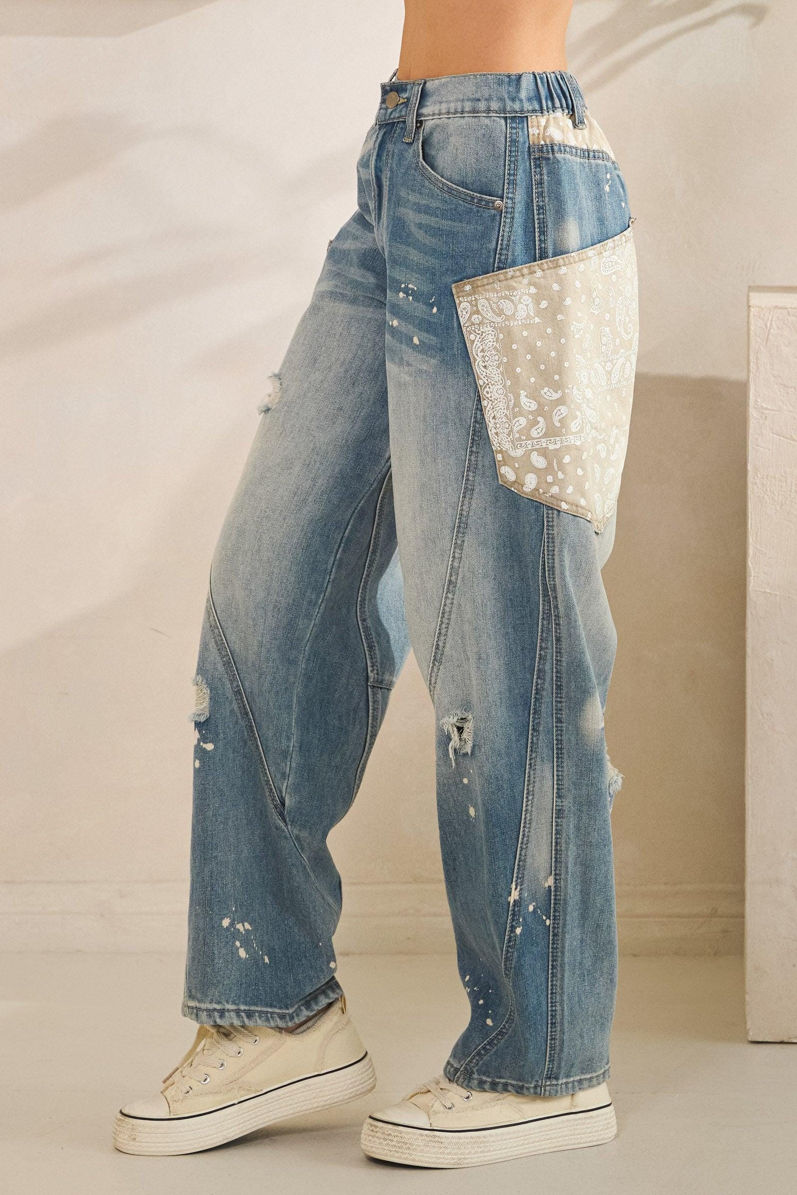 Wide leg opening of grunge-inspired denim trousers with paint splatter details and rugged frayed edges