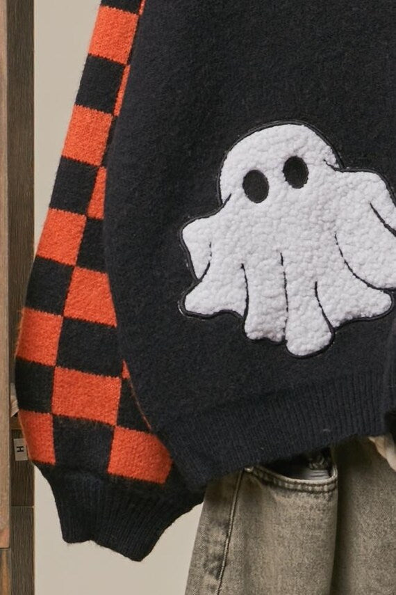 Flat lay of the spooky orange and black checkerboard ghost sweater arranged with Halloween accessories