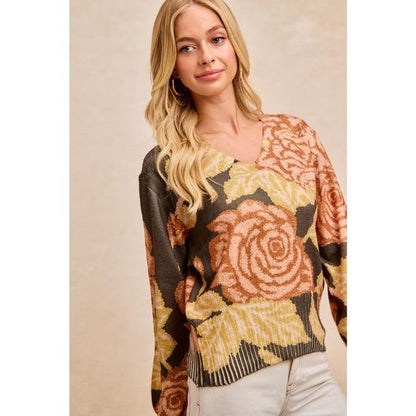 Woman wearing a V-neck dark floral knit sweater in olive, peach, and golden yellow with balloon sleeves.