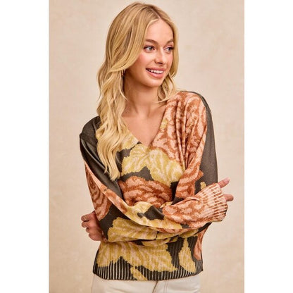 Blonde woman wearing a dark floral knit V-neck sweater with balloon sleeves in olive green, peach, and yellow.