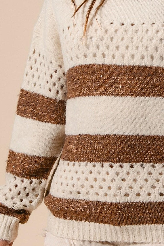 Close-up of a women's cream and brown striped knit sweater featuring a perforated open-stitch pattern.