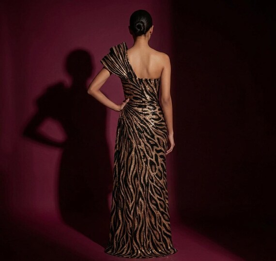 Back view of a women's one-shoulder sequined mermaid gown in a shimmering bronze and black zebra print.