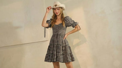 Women's brown gingham mini dress featuring puff sleeves, a shirred bodice, tiered skirt, and styled with a cowgirl hat.