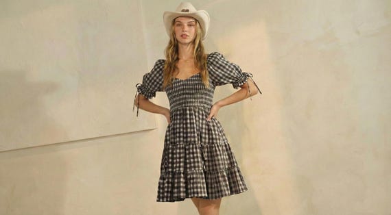 Woman in a black gingham puff sleeve mini dress with a shirred bodice and tiered skirt, wearing a western cowboy hat.
