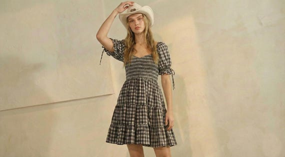 Model in a black gingham puff sleeve mini dress with a shirred bodice, tiered skirt, and coastal cowgirl hat.