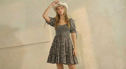 Model in a black gingham puff sleeve mini dress with a shirred bodice, tiered skirt, and coastal cowgirl hat.