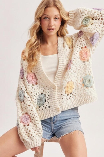 Cottagecore ivory open-stitch crochet cardigan with pastel 3D floral appliqués, balloon sleeves, and a relaxed fit.