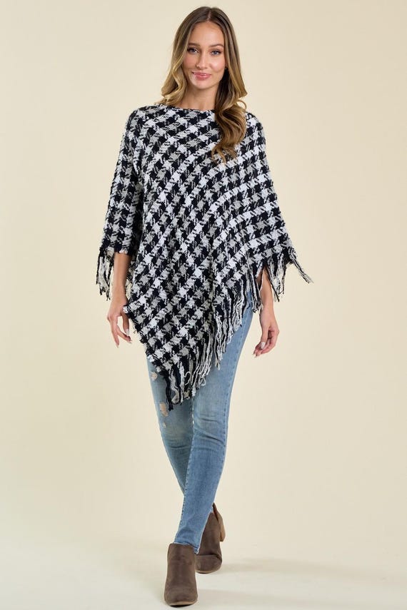 Women's black and white houndstooth print knit poncho with an asymmetric drape and fringe trim.