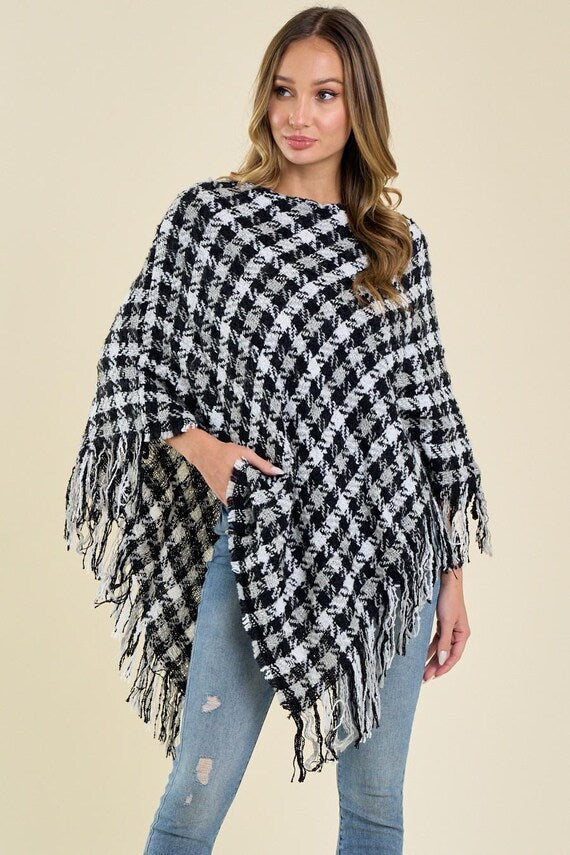 Women's black and white houndstooth knit poncho with an asymmetric drape and fringe trim.