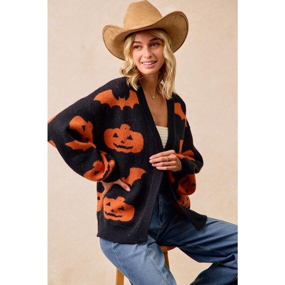 Women's cozy Whimsigoth black open-front knit cardigan with bold orange pumpkin and bat print, relaxed fit, generous sleeves.