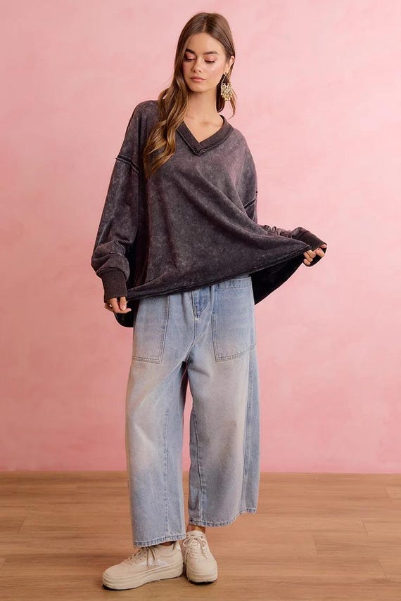 Oversized mineral wash charcoal sweatshirt with V-neck and raw seam detailing, paired with light wash wide-leg jeans.