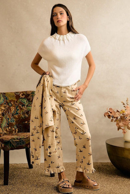 Model wears cream wide-leg cotton denim pants with a mallard duck print and ruffle hem in a cottagecore style.
