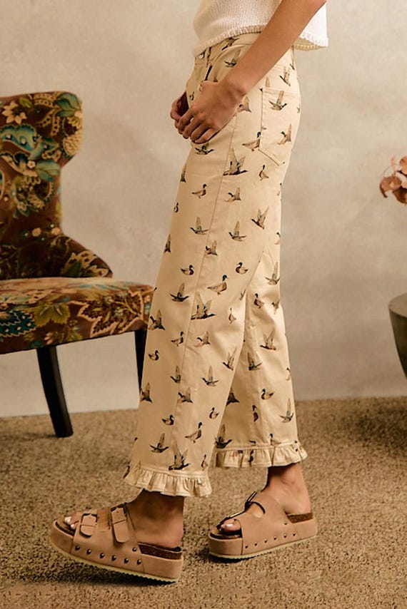 Side view of cream cottagecore wide-leg cotton denim pants with a flying mallard duck print and ruffled hem.