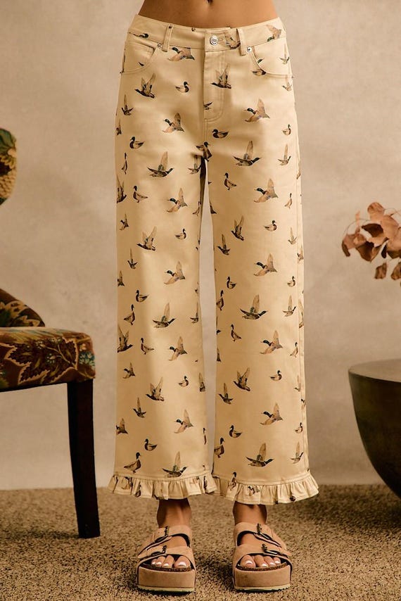 Cream cotton denim cottagecore wide leg pants featuring an all-over flying duck print and a ruffle hem at the ankle.