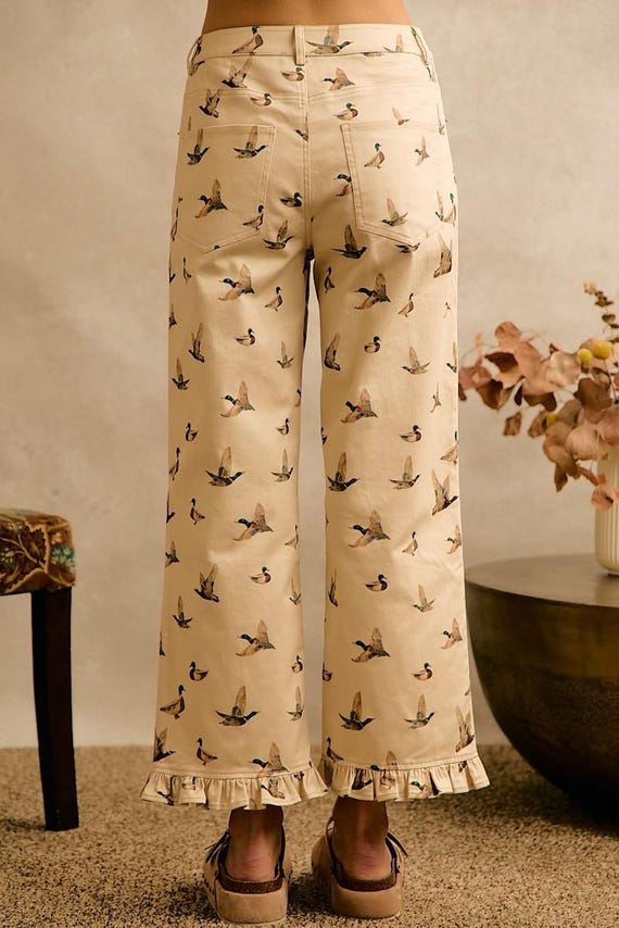 Back view of women's cottagecore cream cotton denim wide leg pants featuring an allover mallard duck print and ruffle hem.