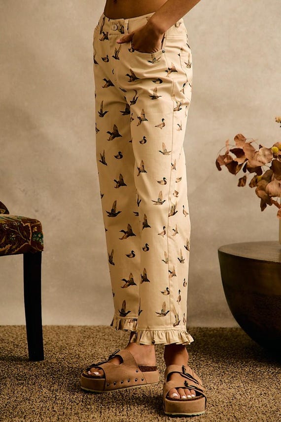 Cottagecore cream cotton denim wide leg pants with an allover mallard duck print and a ruffle hem at the ankles.