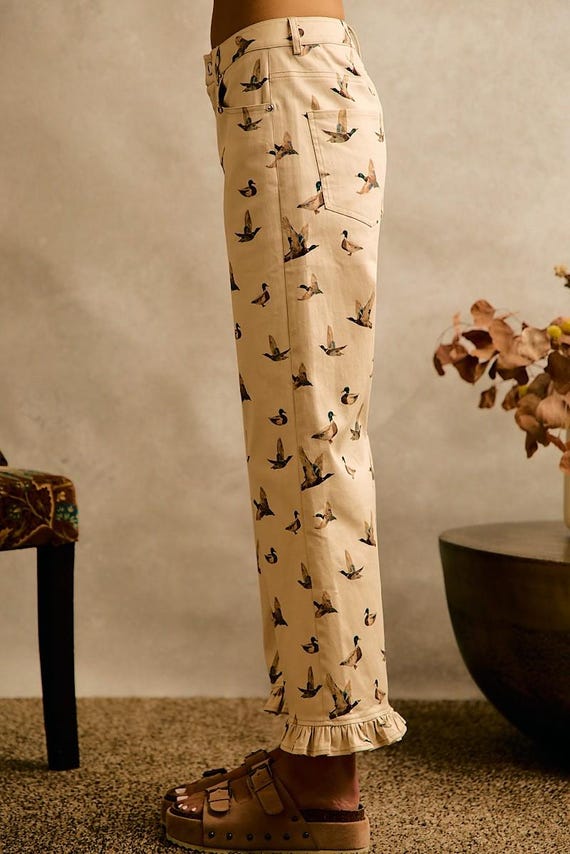 Side view of cream cottagecore cotton denim wide leg pants with an all-over mallard duck print and a ruffle hem.